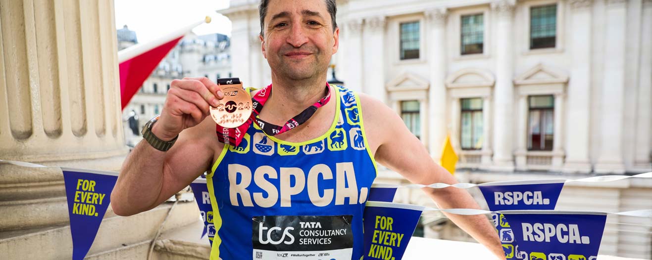 A man showing his finishers' medal after completing the London Marathon nwearing his RSPCA vest.