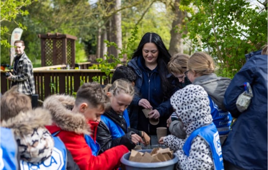 A teacher and group of students surround a table in the woodland, carrying out a craft activity.