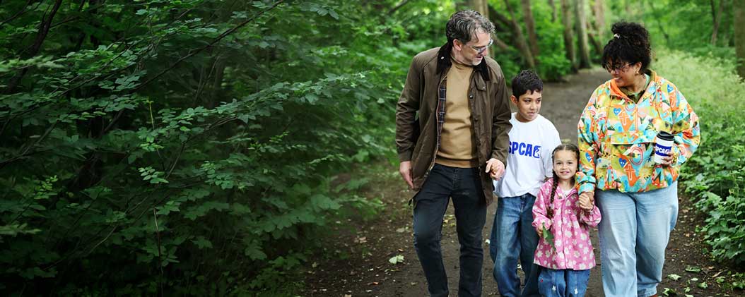 A family of four walks happily along a leafy woodland path.