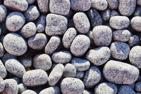Grey pebbles piled together in the sun. 