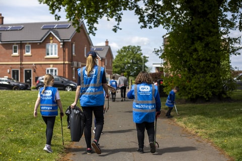 A woman and two children wearing a blue RSPCA bib picking litter in a residential area. 