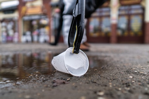 A white plastic cup being picked up off the ground by a litter picker.