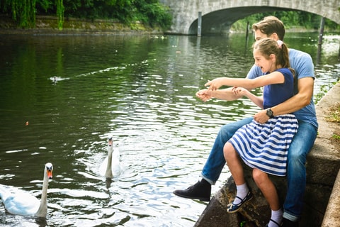 A father and his daughter feeding waterfowl next to a river.