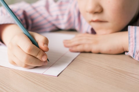 A young child writing on a sheet of blank paper on a desk. 
