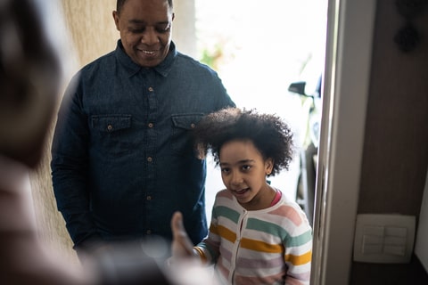 A father figure and child stood in doorway conversing with another person. 