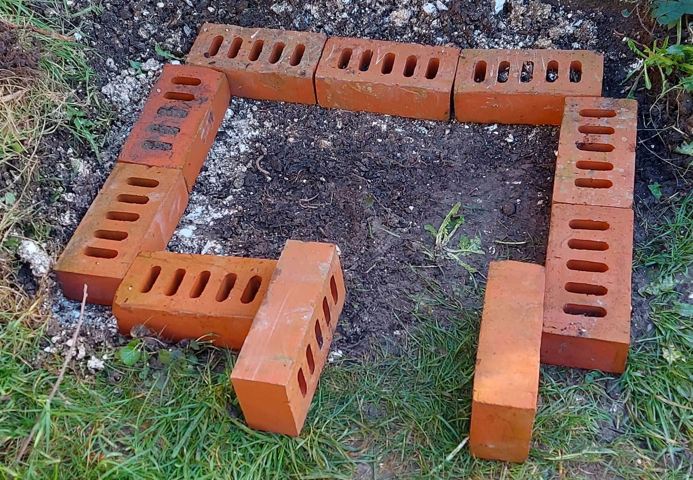 Single set of bricks on the ground to create an outline chamber and tunnel for a hedgehog house.