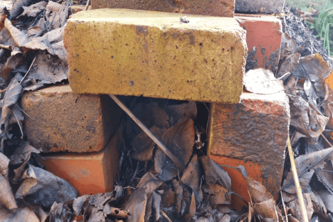 A close up image of stacked bricks on the ground to form an entrance. A stick is leaning in the entrance to form a barrier.