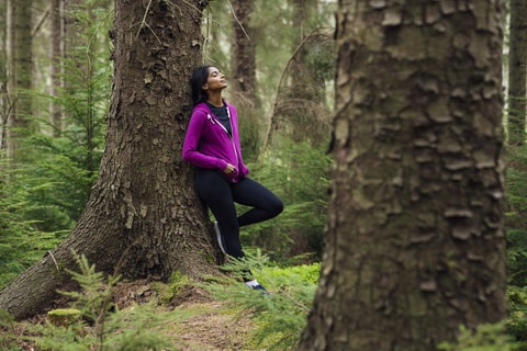 Young person feeling calm in a woodland while resting against a tree.