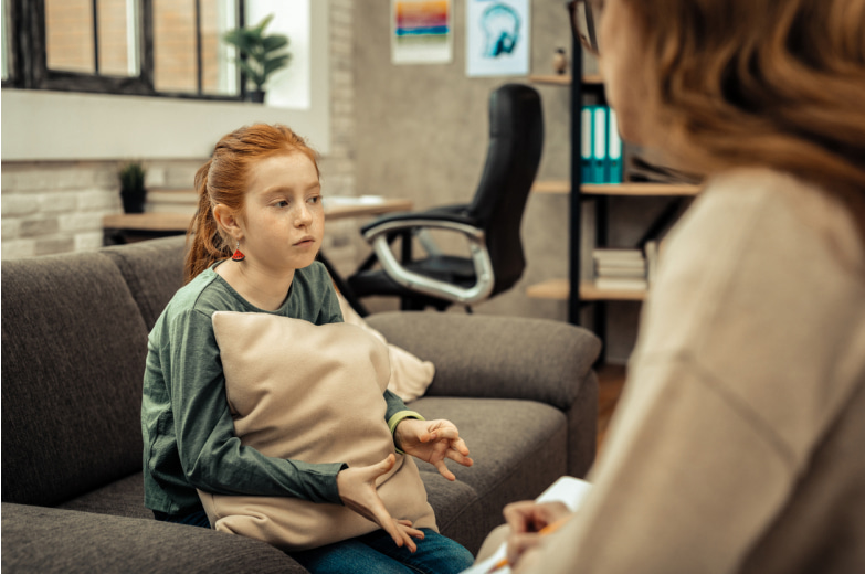 A young girl talking to a parent, on a couch