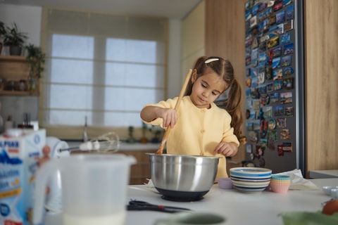 A child in a kitchen stirring food in a metal bowl.