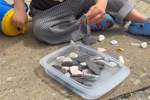 A young child placing small rocks and stones into a plastic container.