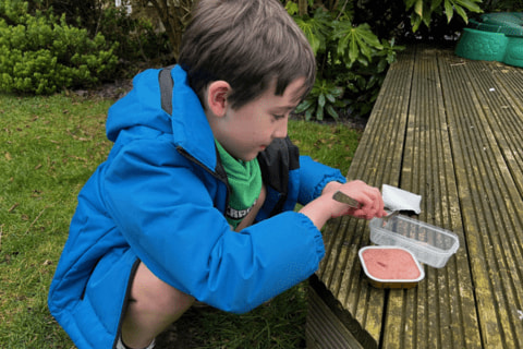 A young child spooning food into a plastic container.