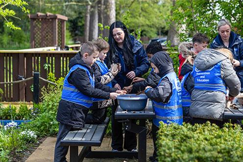 A group of children wearing RSPCA tabards in a garden, two adults are assisting