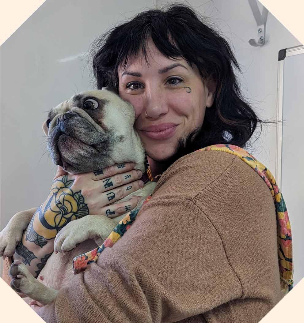 A young woman cuddling a dog and smiling to camera.