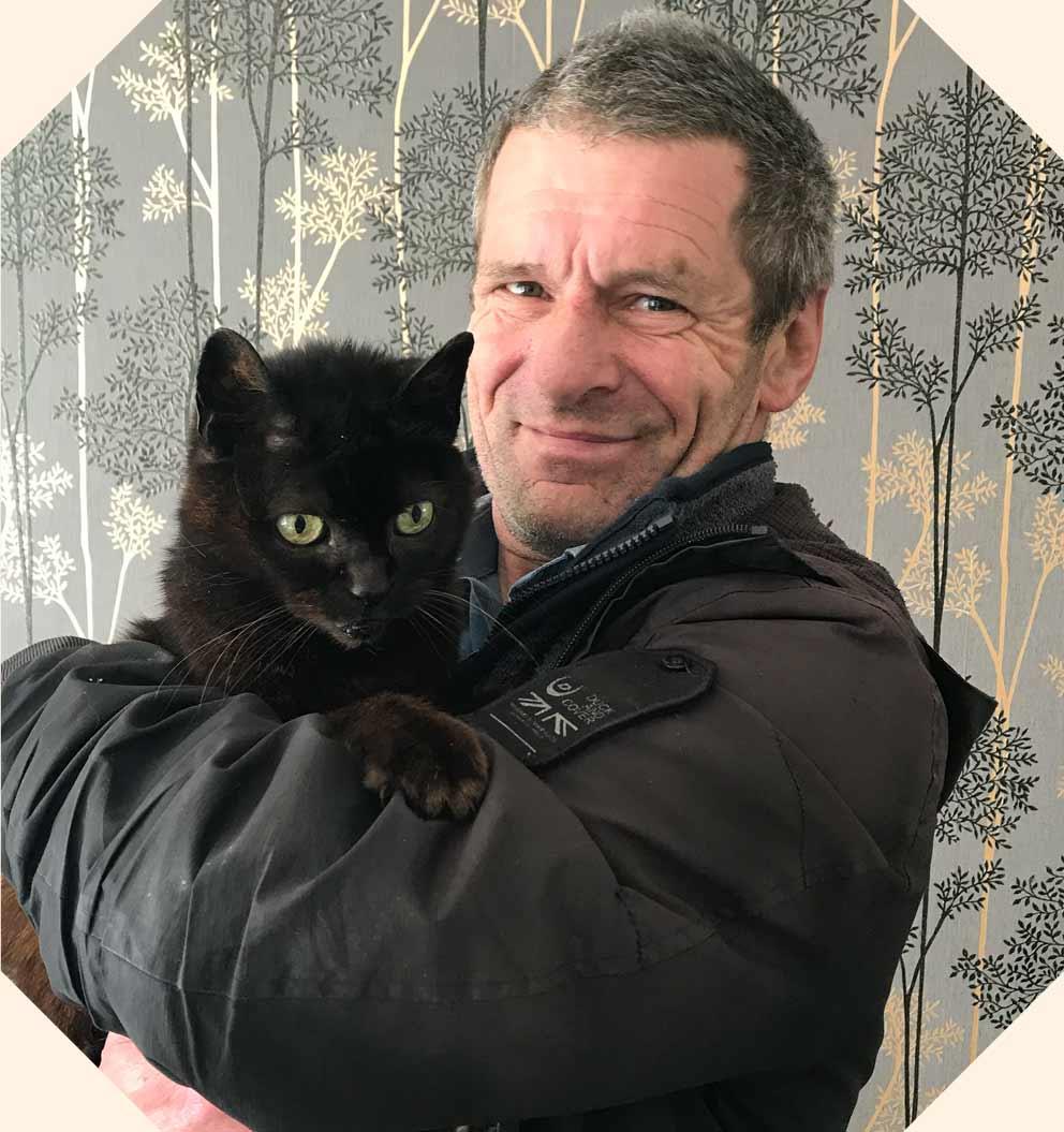 A smiling man holding a black cat.