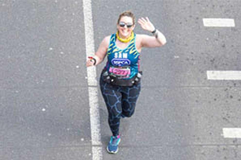 An RSPCA fundraiser running and waving wearing a Team Animal running vest.