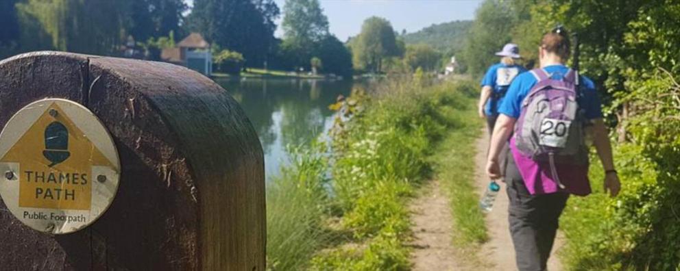 Two walkers wearing rucksacks walking along side the Thames public footpath.