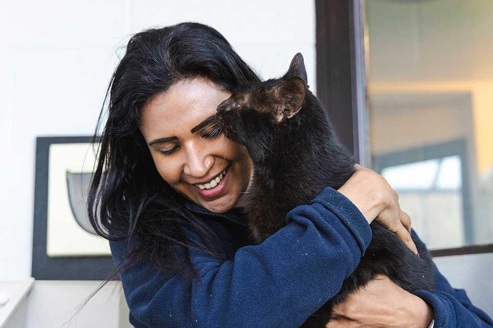 RSPCA inspector cuddling a black cat and smiling.