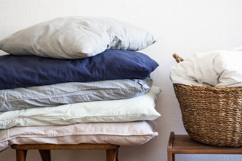 Pillows stacked neatly on a stool next to a wicker basket.