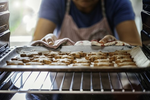 A woman placing star-shaped dog treats in the oven to bake.