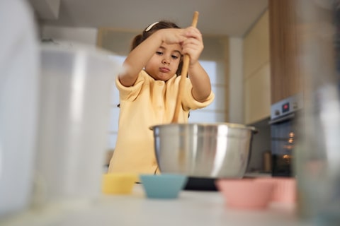 A young child in a kitchen combining ingredients in a bowl. 